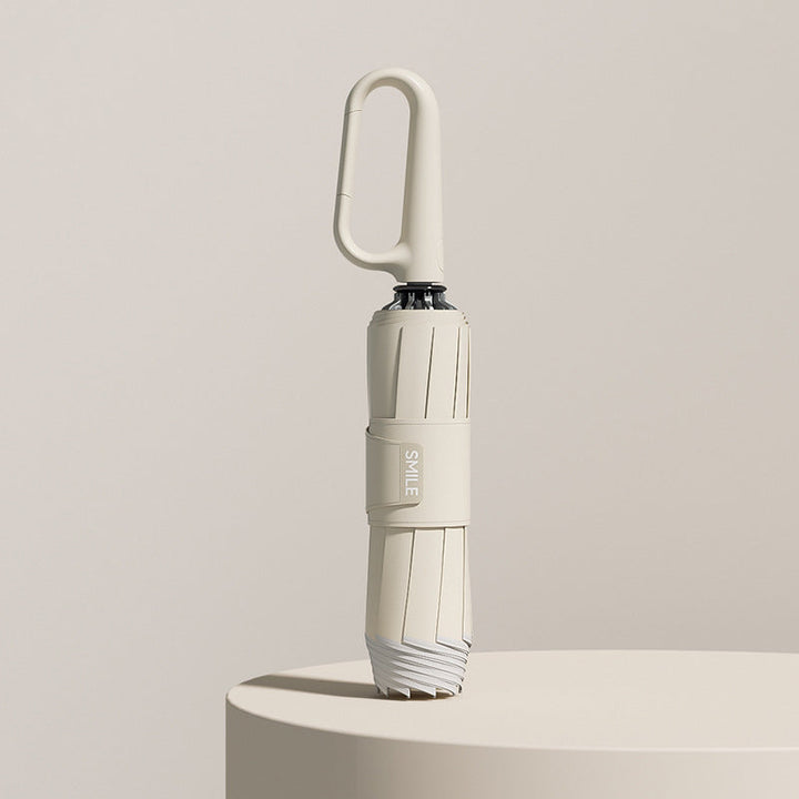 Beige hopfällbart reseparaply med karbinhakehandtag stående på piedestal