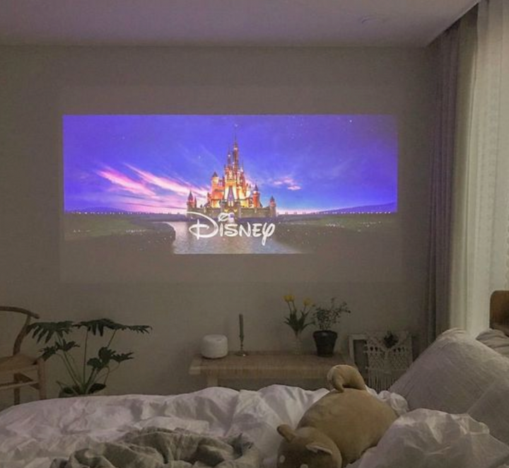 Mini filmprojektor som visar en film på en vit sovrumsvägg