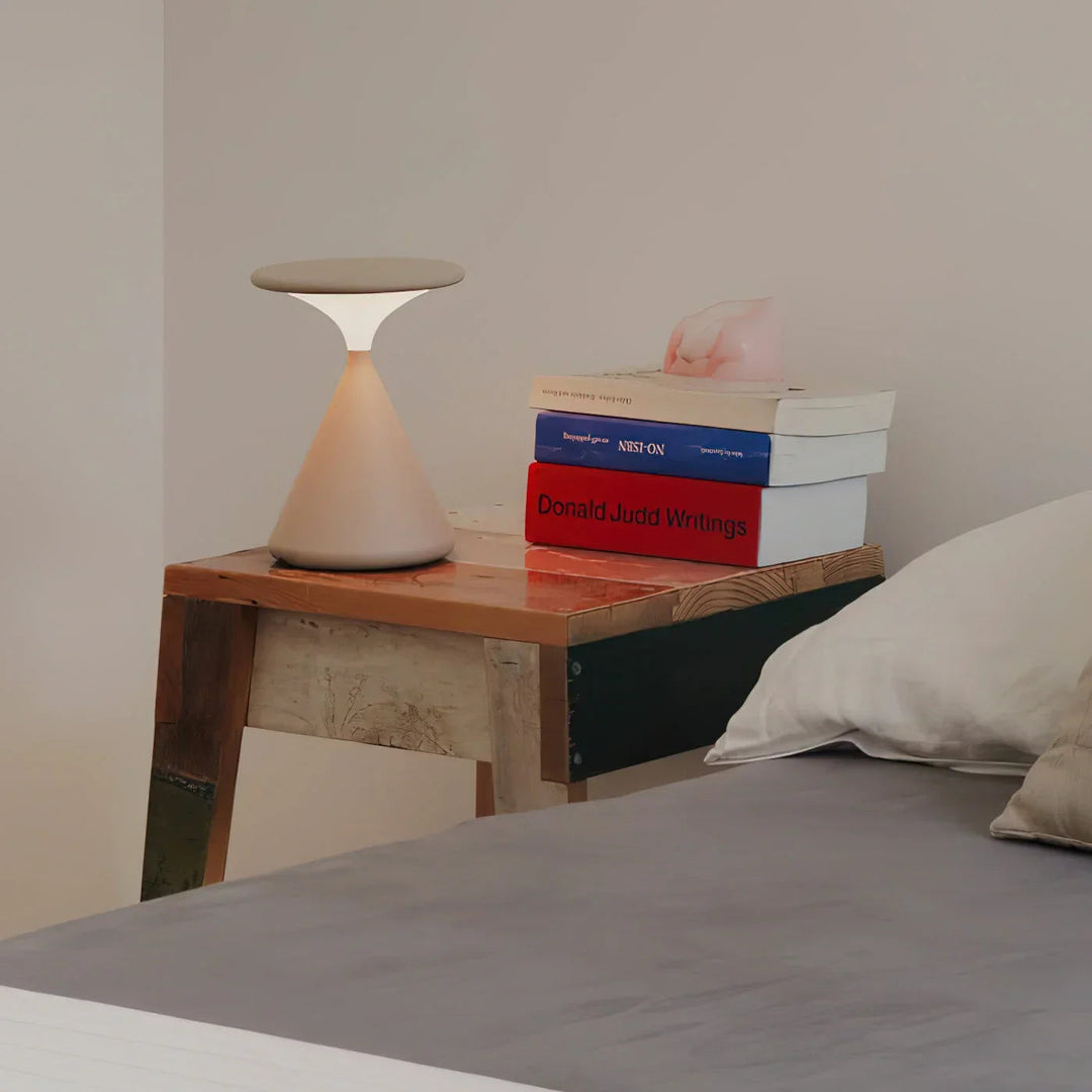 LuminaHour trådlampa med timglas på ett nattduksbord bredvid böcker och säng