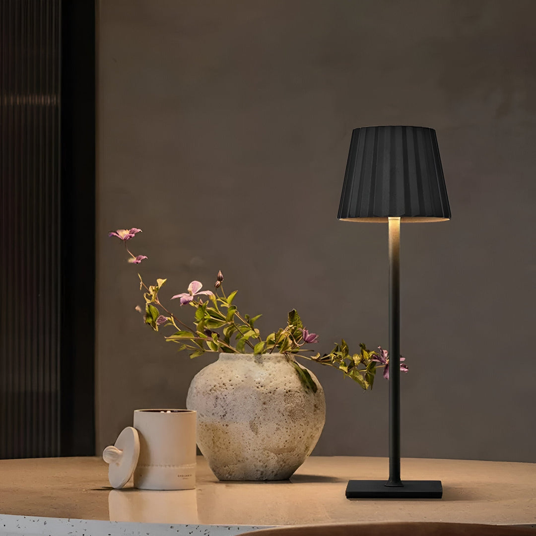 Svart trådlös bordslampa placerad på ett bord bredvid en vas med blommor