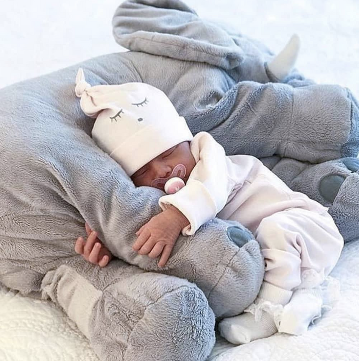 En nyfödd baby sover tryggt mot en stor grå elefantkudde i plysch.