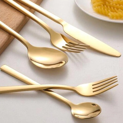 Gyllene bestickset i rostfritt stål med kniv, gaffel och skedar på träskiva