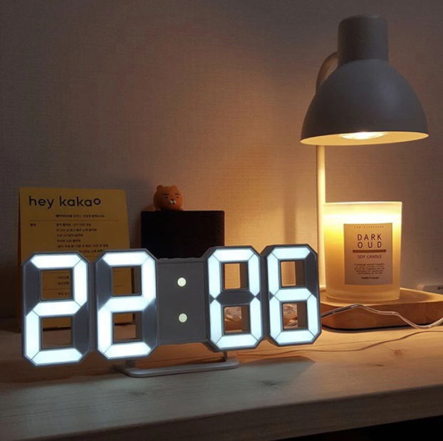 Smart 3D digital klocka upplyst på nattduksbord bredvid lampa