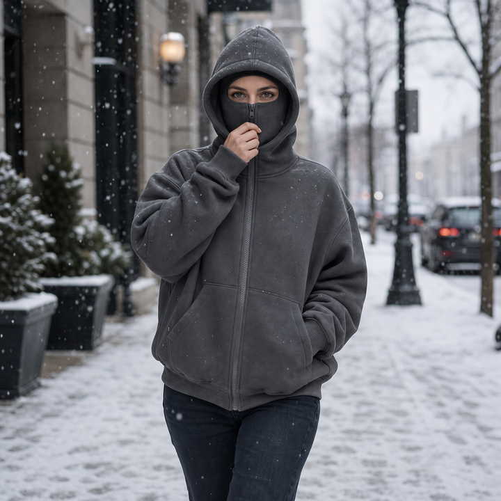 Mörkgrå huvtröja med dragkedja och integrerat ansiktsskydd på snöig stadsgata