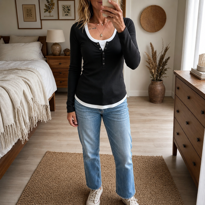 Kvinna i svart långärmad damtopp med lager-på-lager-design och jeans i ett rum