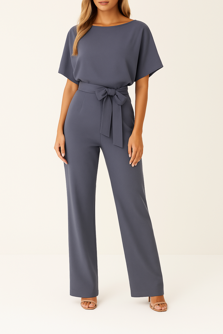 Minimalistisk damjumpsuit med flytande vida ben, kort ärm och dekorativa knytband.