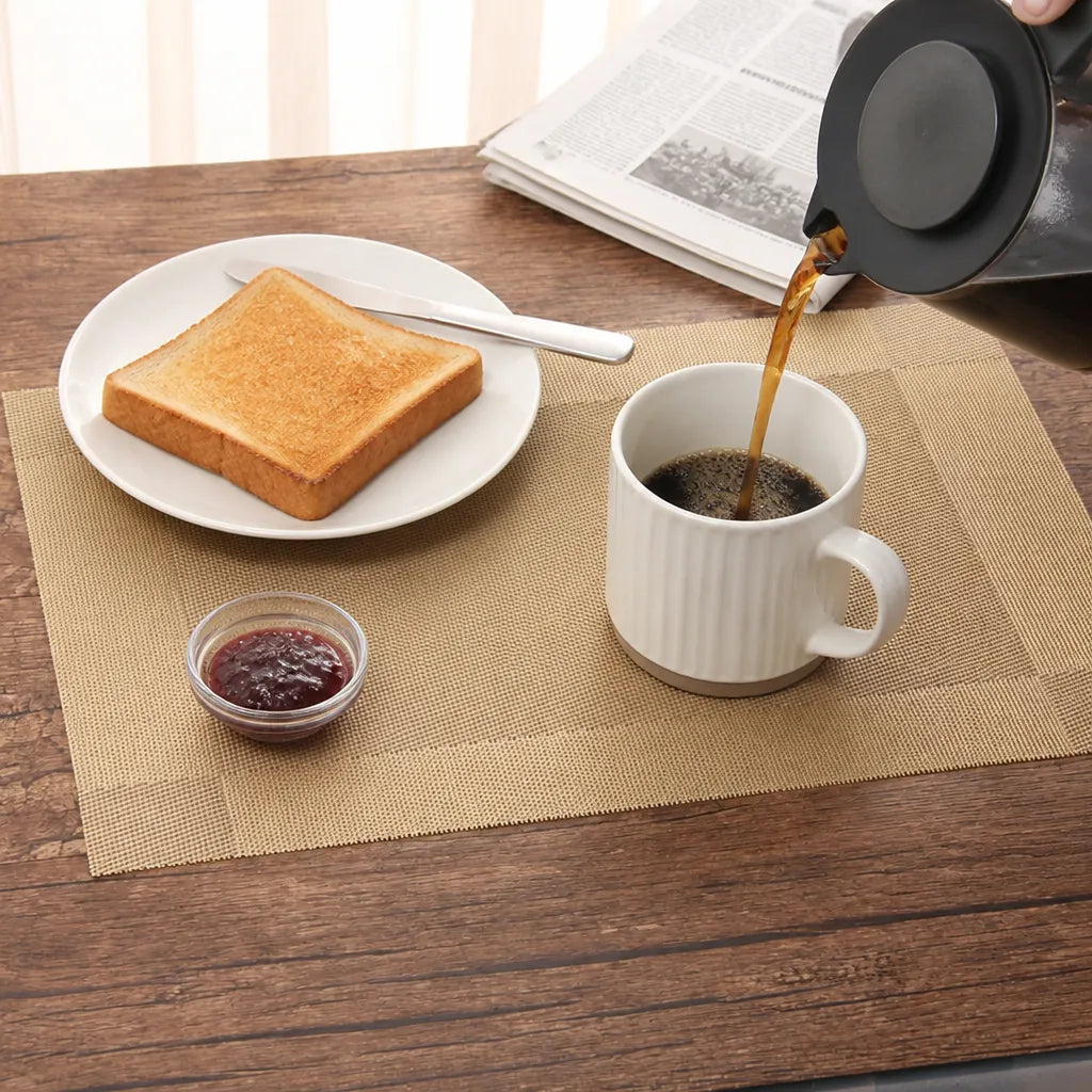 Kaffekanna häller kaffe på ett beige Wovella bordsunderlägg med rostat bröd