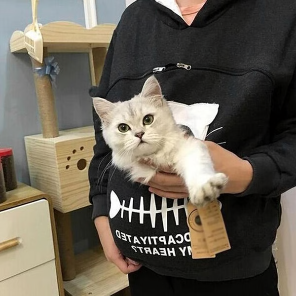 Svart kattpåse hoodie på person som håller en ljus katt nära bröstet