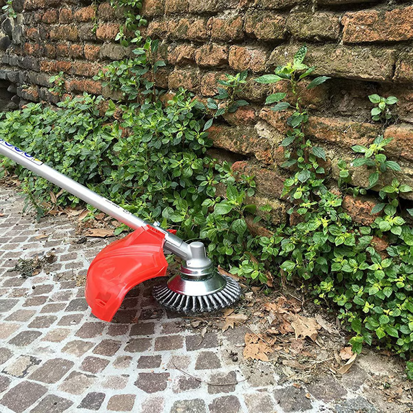 Ogräsborste i kolfiberstål som används längs en tegelvägg på stenläggning
