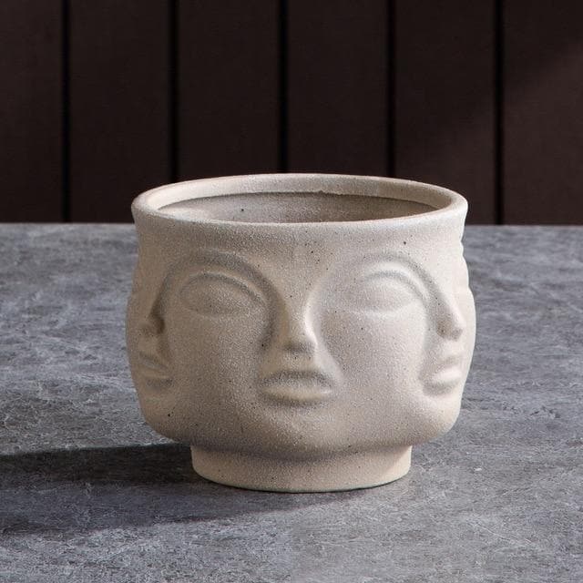 Beige skulptural keramisk blomkruka med ansiktsmotiv på stengolv