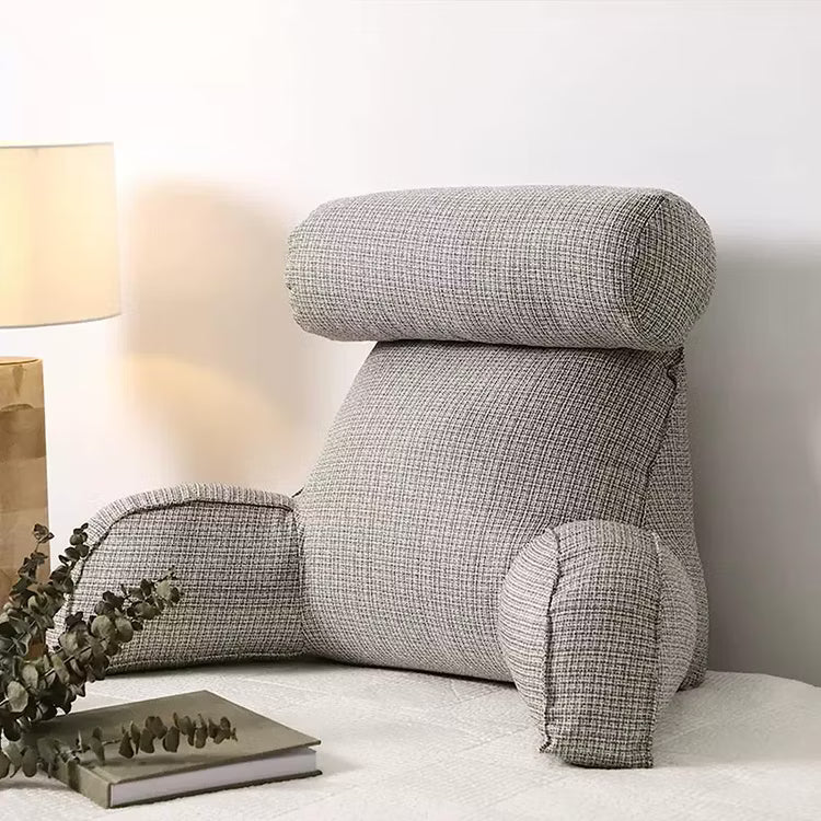 Grå läskudde uppställd i sängen bredvid en bok och lampa