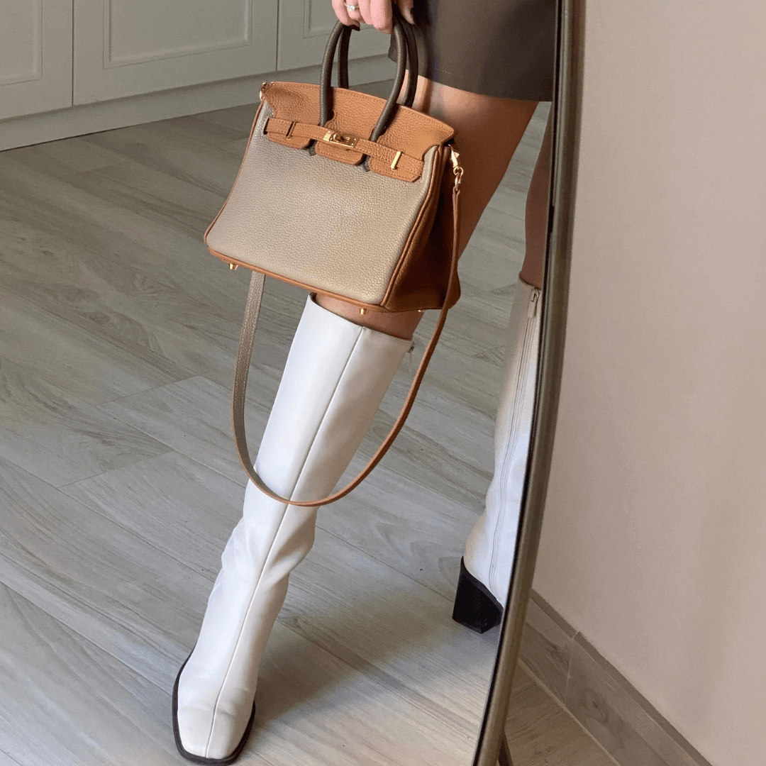Handväska Élise i beige buren med axelrem mot spegel
