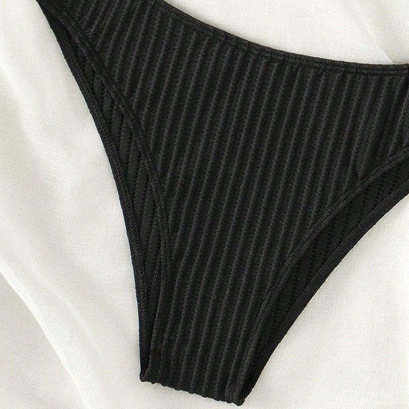 Närbild: Högskurna ribbade bikini-trosor i svart för dam. Del av ett triangelbikini-set för stranden.