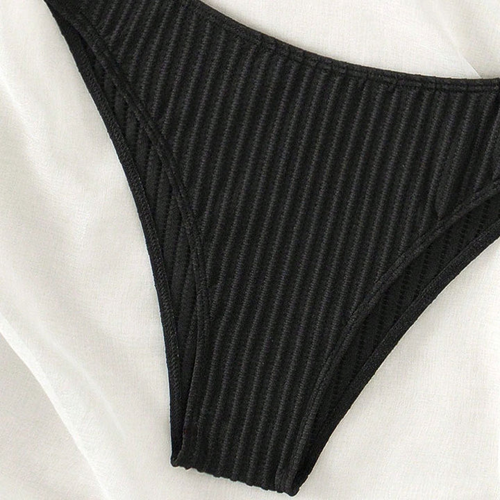Närbild: Högskurna ribbade bikini-trosor i svart för dam. Del av ett triangelbikini-set för stranden.
