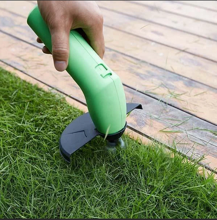 Närbild på grön grästrimmer som klipper gräs bredvid trädäck