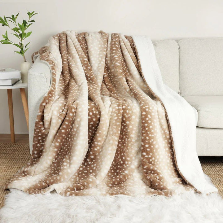 Vändbar beige pläd med hjortmönster draperad över en ljus soffa