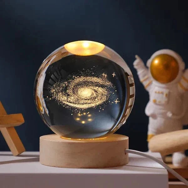 3D kristallkula med galaxmotiv på träbas med varmt LED-ljus