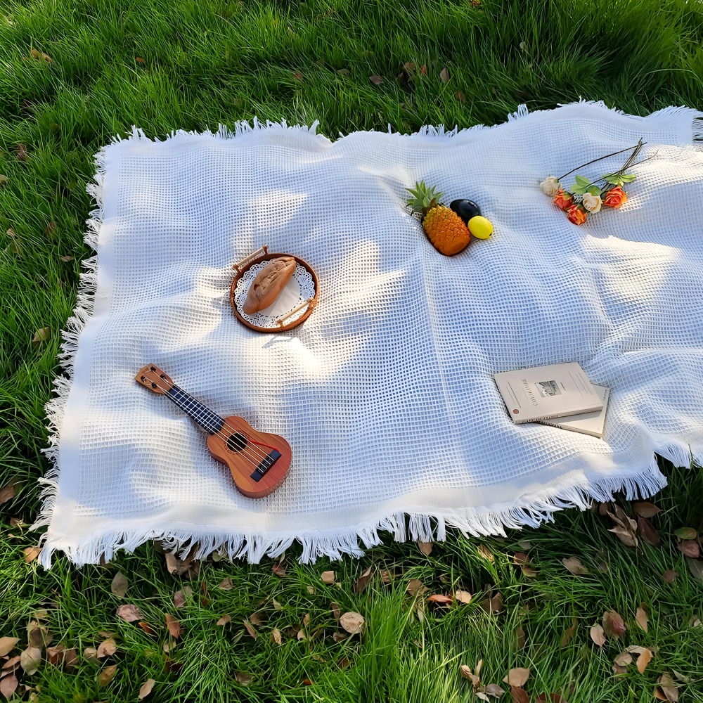 Mjuk vit picknickfilt i bomullsblandning med bohemiska tofsar, idealisk för avkoppling utomhus.