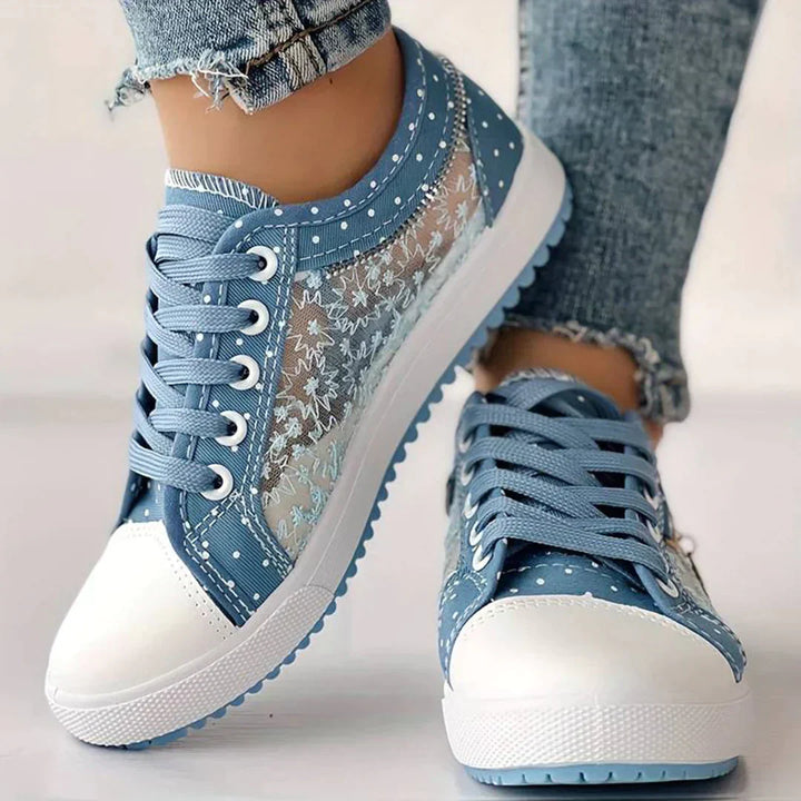 Närbild på vita damsneakers med blommig spets, visar detaljer av elegant design och snörning.