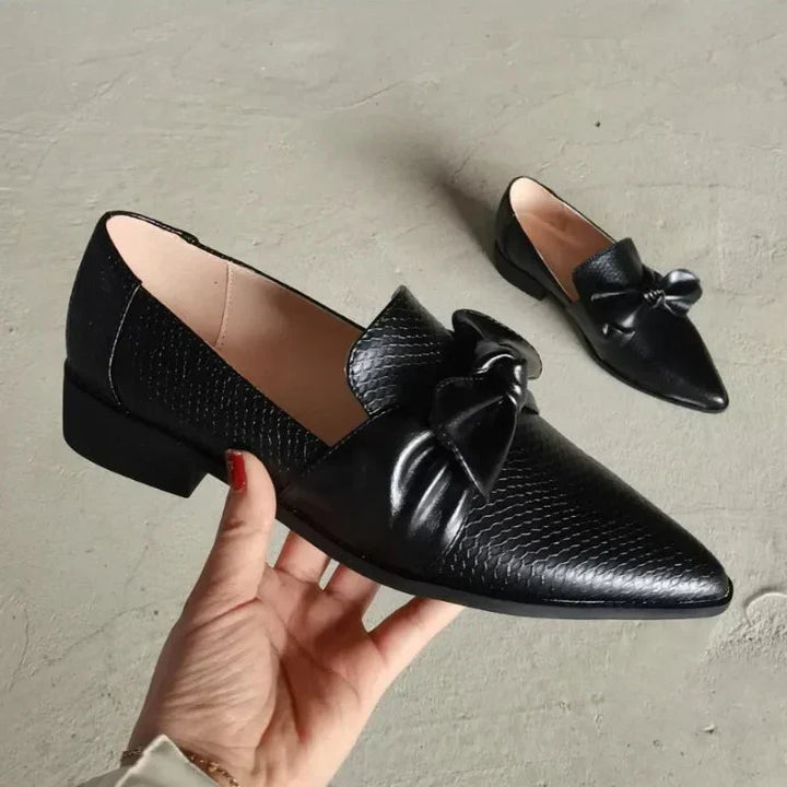Detaljbild på dekorativ rosett och spetsig tå på svarta damloafers